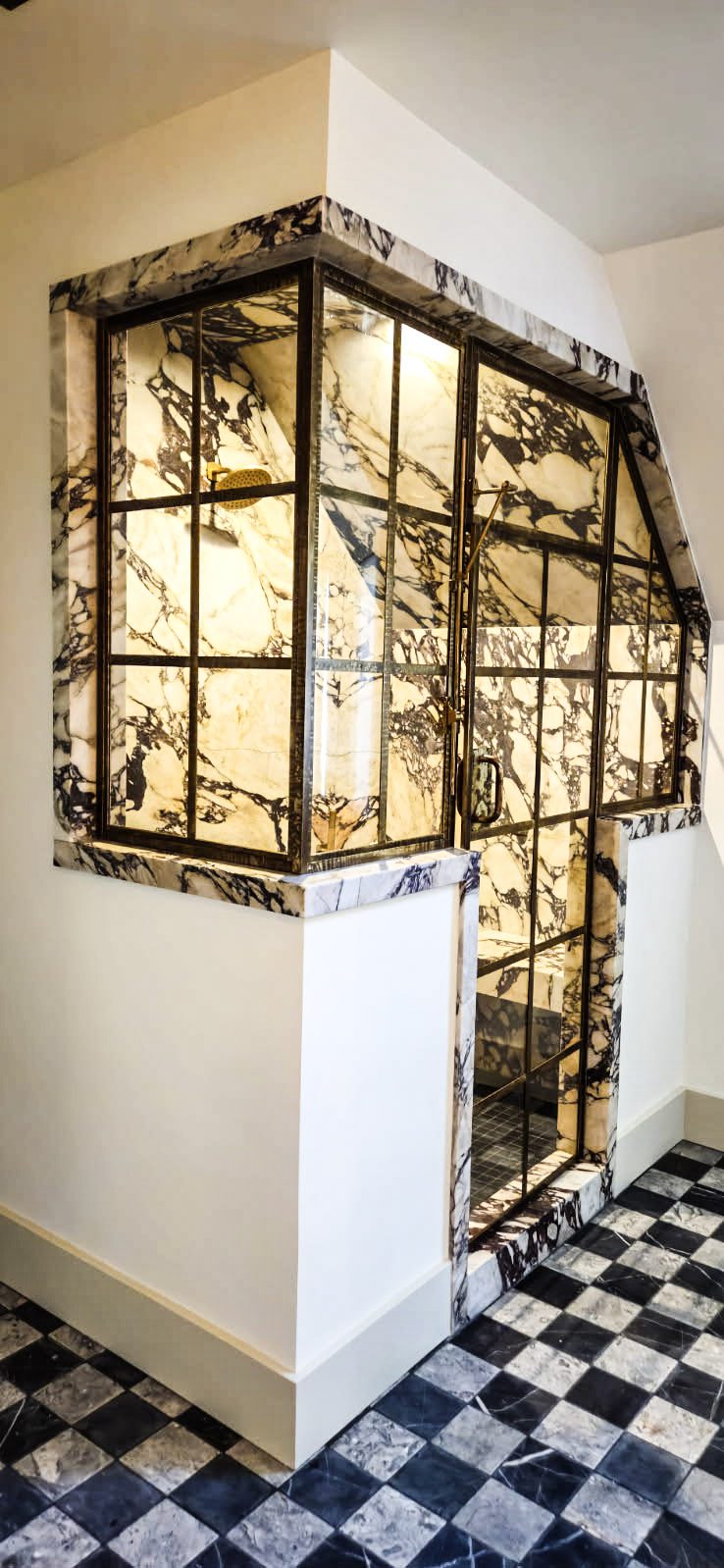 Brass-framed glass shower enclosure set in marble