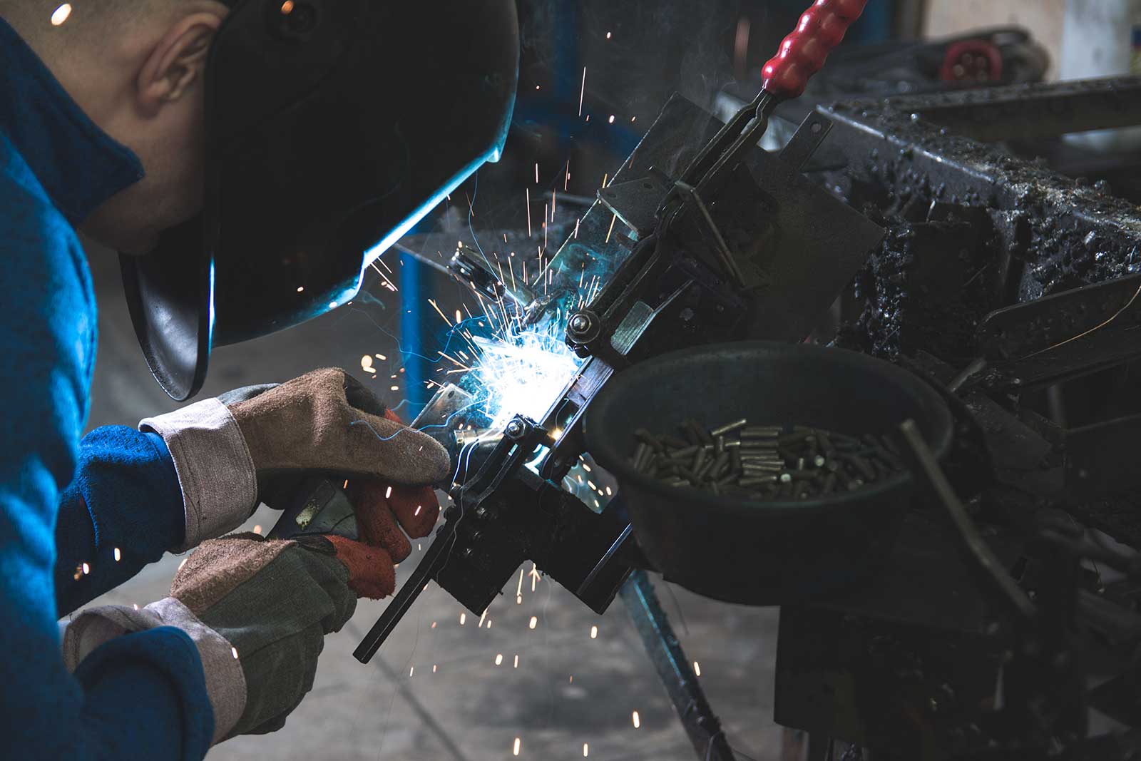 Welder working on a steel assembly with sparks at the joint